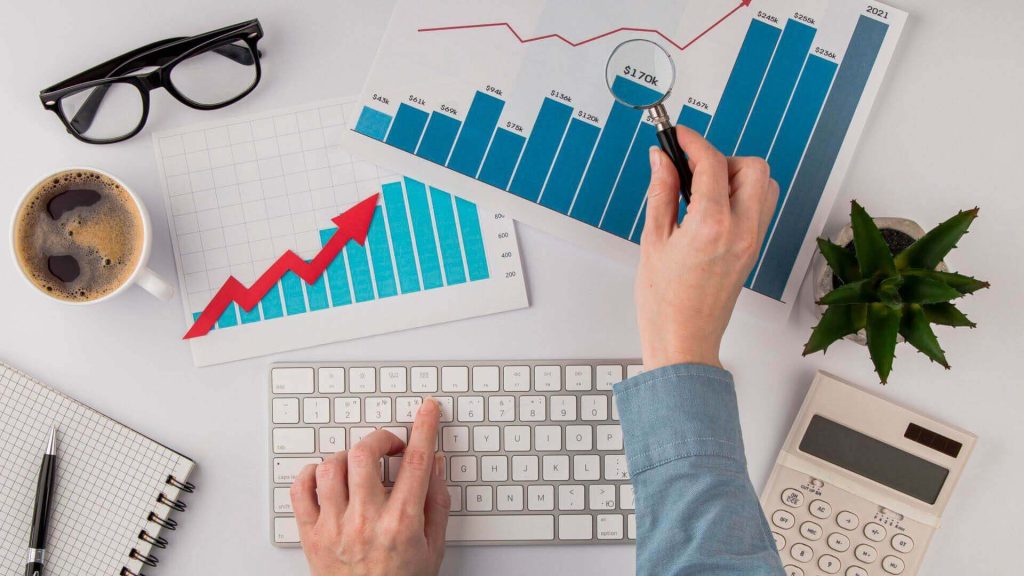 Person analyzing business growth charts on a desk with a keyboard, coffee, and calculator